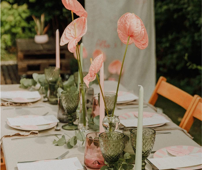 Mesa de boda decorada con anturios rosas, copas de cristal verde y rosa, velas altas en tonos pastel y vajilla con platos de rayas rosa.